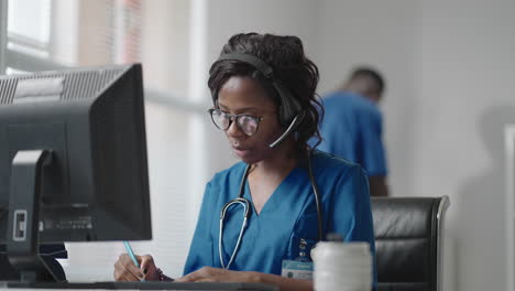 Die-Afrikanische-Medizinische-Assistentin-Trägt-Ein-Weißes-Kittel-Headset-Und-Ruft-Einen-Entfernten-Patienten-Am-Computer-An.-Arzt-Spricht-Mit-Klient-über-Virtuelle-Chat-Computer-App.-Telemedizinische-Ferngesundheitsversorgung
